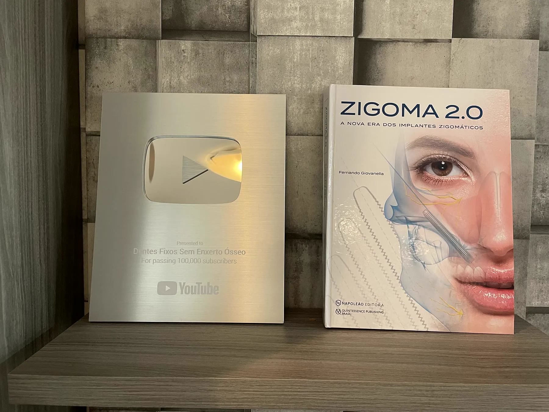 Placa de 100 mil inscritos do YouTube ao lado do livro Zygoma 2.0
